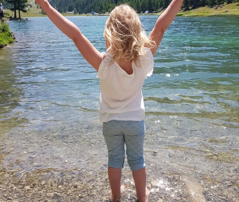 enfant profitant du vent devant lac de montagne