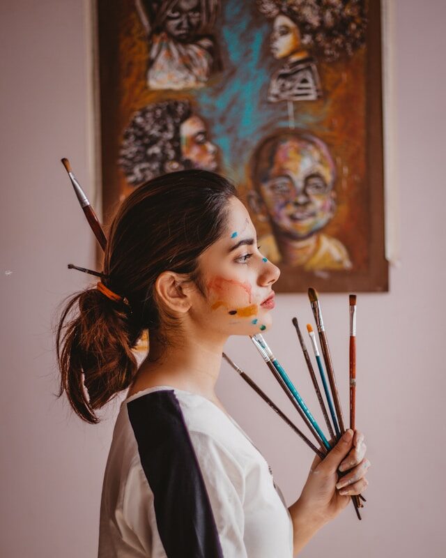 Photo by Muhammad Rahim Ali a woman holding a bunch of paint brushes